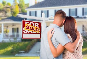 Military Couple Looking At House with Sold For Sale Real Estate Sign In Front.